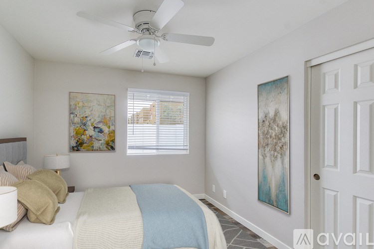 A bedroom with a bed, pillows, a ceiling fan, and a painting on the wall.