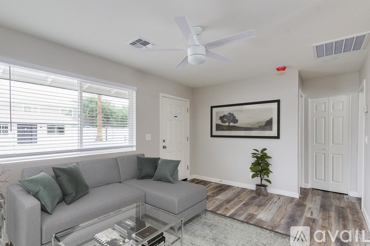 A living room with a grey couch, a glass coffee table, and a ceiling fan.