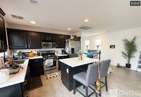 A kitchen with black cabinets and a white island with two chairs.