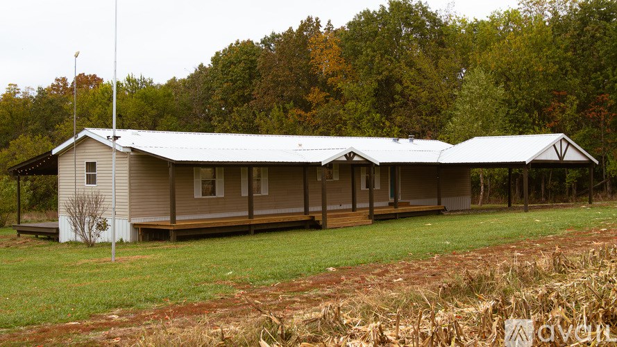 A house with a grey roof and white walls is surrounded by a grassy area and trees.