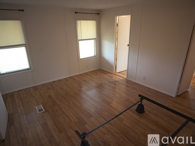 A room with wooden floors and white walls, with a window and a door visible.