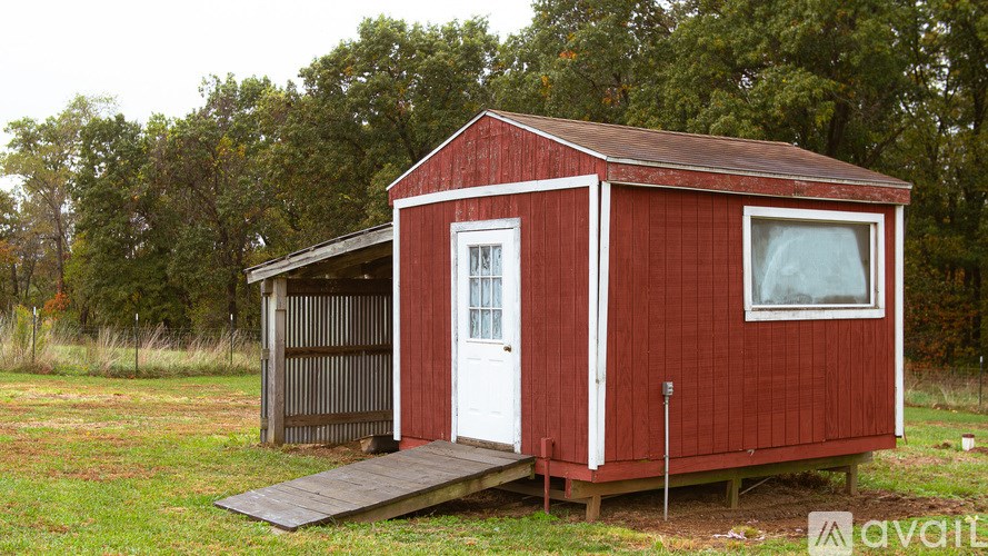 A red house with a white door and a window is in the grass.
