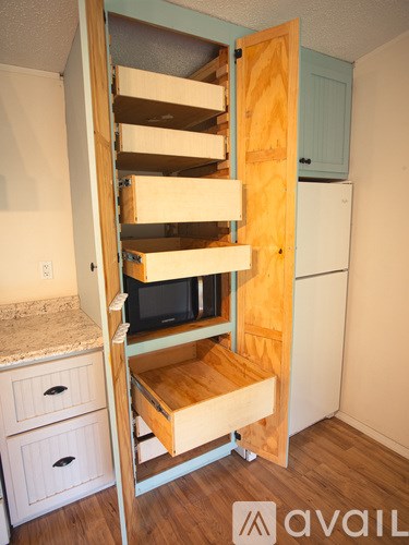 A wooden shelving unit with a microwave on the bottom shelf is open.