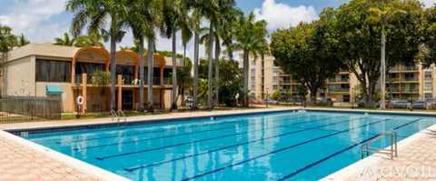 A large swimming pool surrounded by palm trees and apartment buildings.
