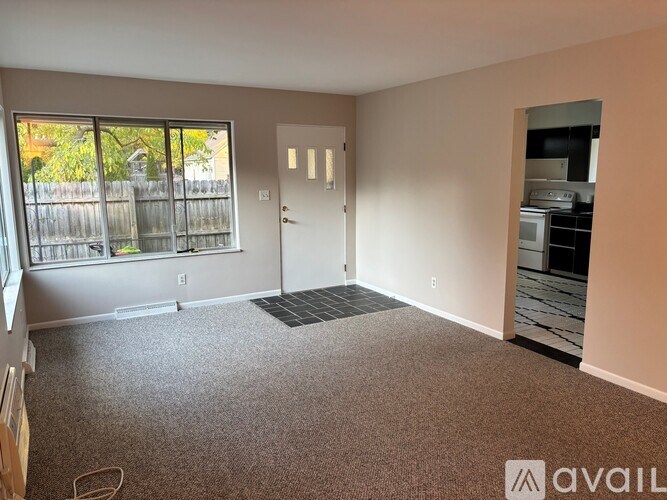 A spacious living room with a large window and a door leading to another room.