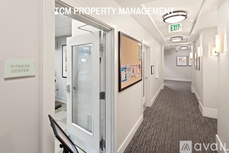 A hallway with a fitness center sign on the left and an exit sign on the ceiling.