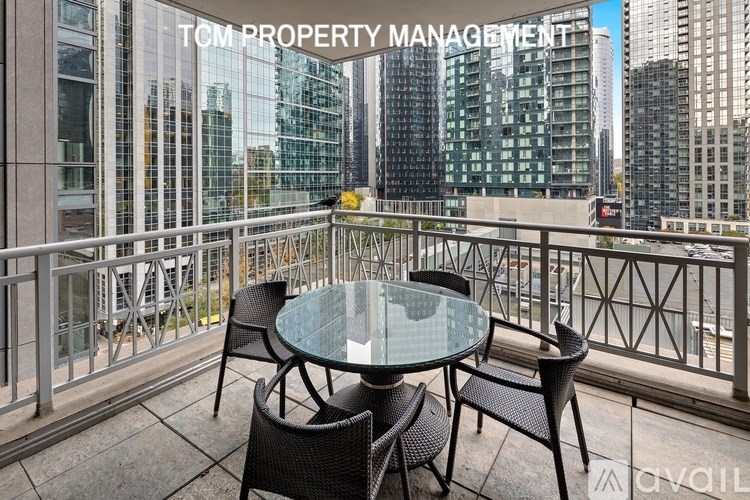 A balcony with a glass table and chairs overlooking a cityscape.