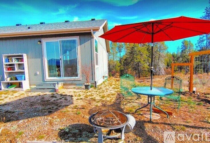 A wooden dining table with chairs and a vase of flowers on top, with a view of the outdoors through the window.