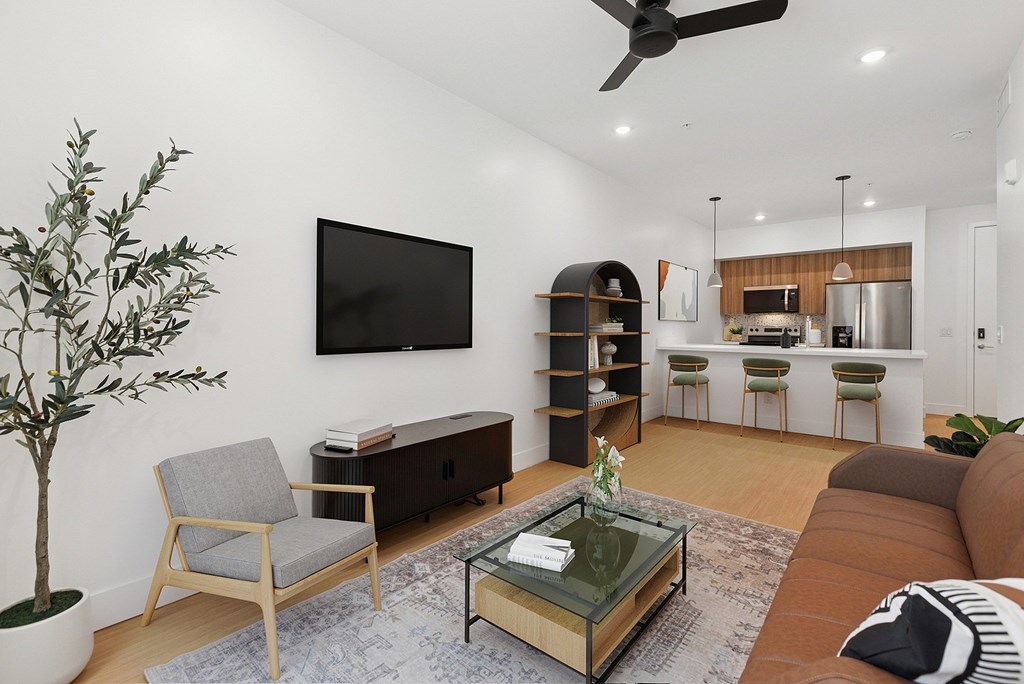 A living room with a grey armchair, a glass coffee table, a brown sofa, a flat screen TV, and a potted plant.