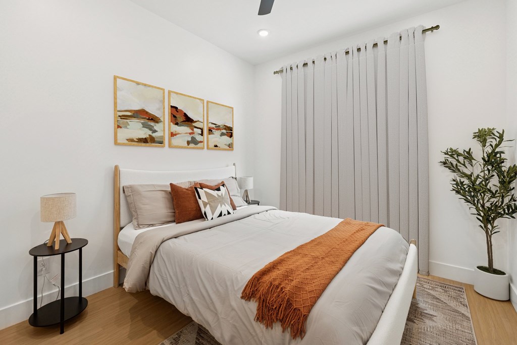 A bedroom with a bed, a lamp, a plant, and pictures on the wall.