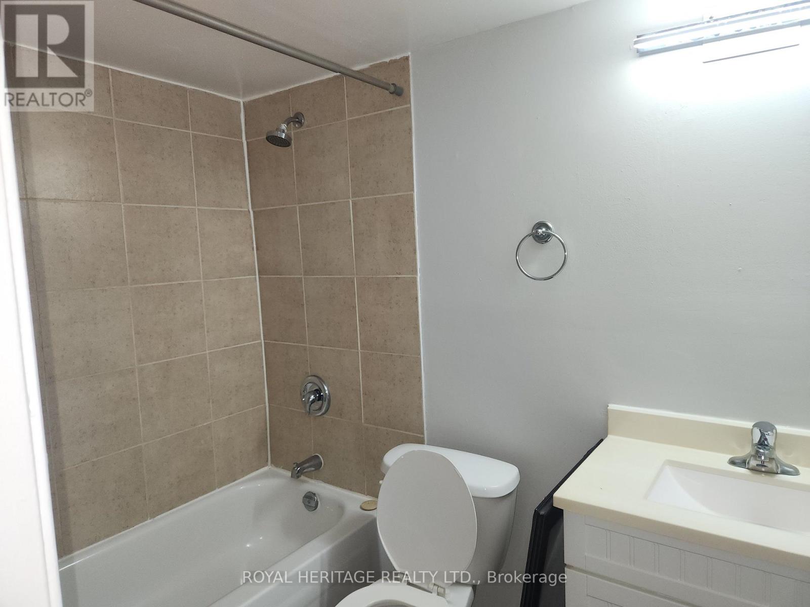 A bathroom with a beige tiled shower, a white toilet, and a white sink.