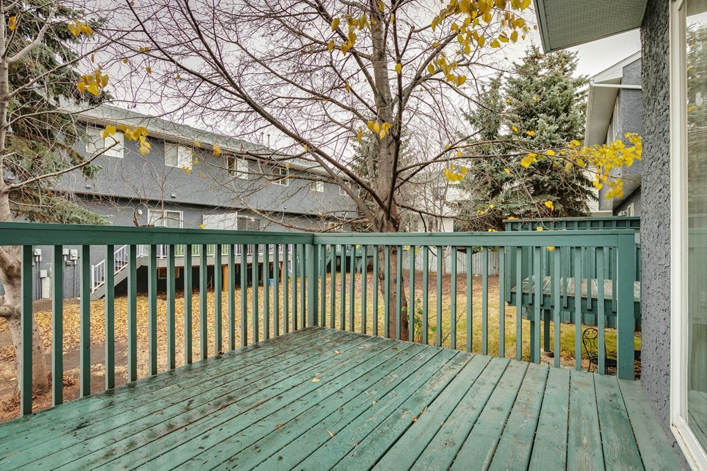 A green wooden deck with a metal railing and a tree in the background.