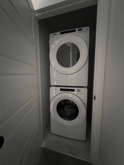 A white washing machine is stacked on top of another in a small, white-walled laundry room.