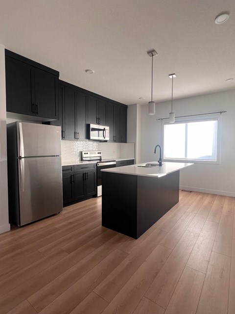A kitchen with black cabinets and a wooden floor.