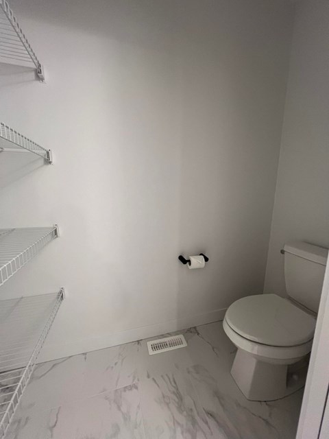 A white toilet sits in a bathroom with a white wall and a white towel rack.