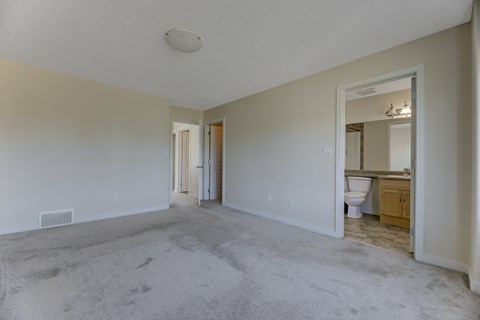 A large empty room with a carpeted floor and a bathroom visible in the background.