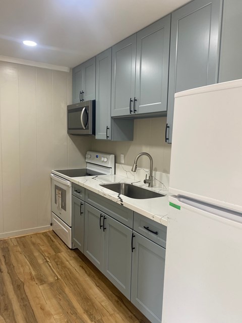 A kitchen with a white fridge, grey cabinets and a white counter top.