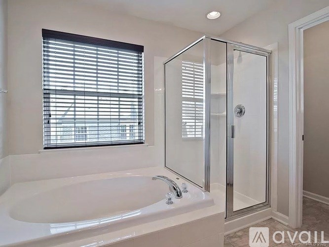A white bathroom with a glass shower stall and a window with blinds.