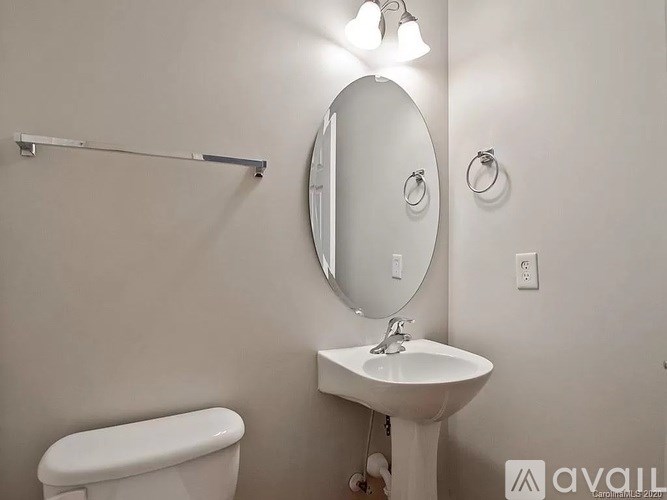 A bathroom with a toilet, sink, mirror, and light fixture.