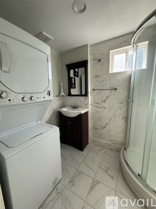A white washing machine is in a bathroom with marble tiles.