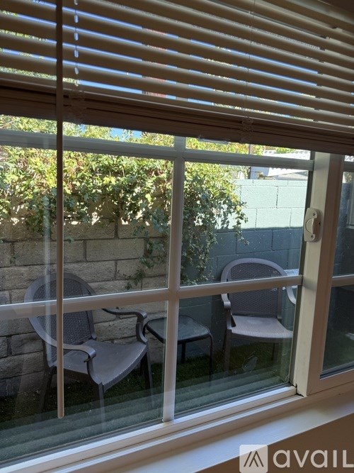 A window with blinds overlooking a patio with a table and chairs.