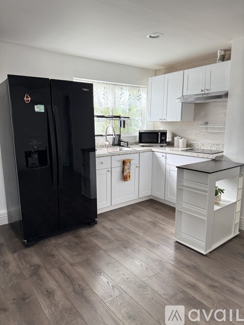 A black fridge in a kitchen with white cabinets and a wooden floor.