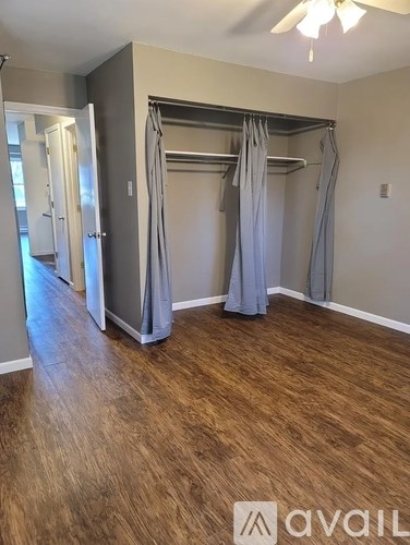 A room with a wooden floor and a bed with grey curtains.