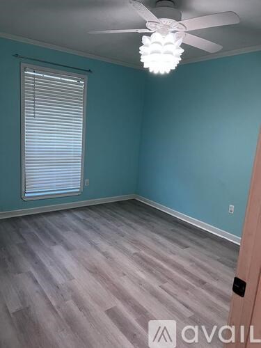 A room with a ceiling fan and light, wooden flooring, and a window with blinds.