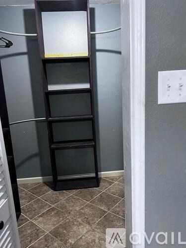 A tall black shelf unit with four shelves is in a room with grey walls.