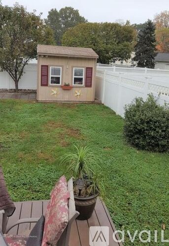 A small shed with a brown roof and red trim is surrounded by a white fence and green grass.