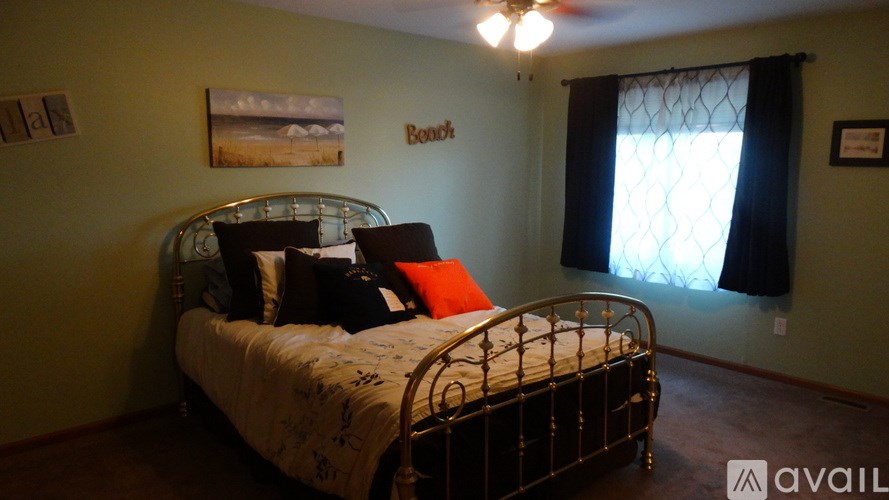 A bedroom with a bed, pillows, a ceiling fan, and a window with a black curtain.