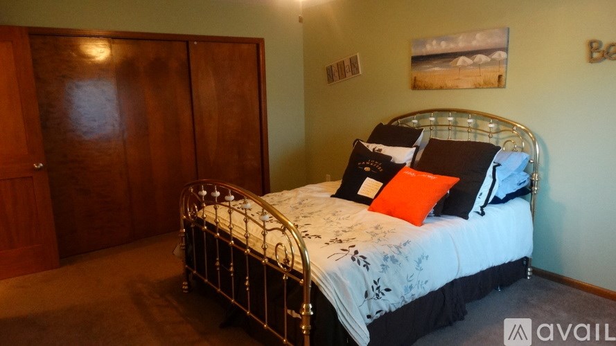 A bed with a white comforter and a metal frame is in a room with a wooden door and a painting on the wall.