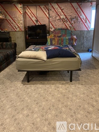 A bed with a blue pillow is in the middle of a carpeted room with a television and a couch.