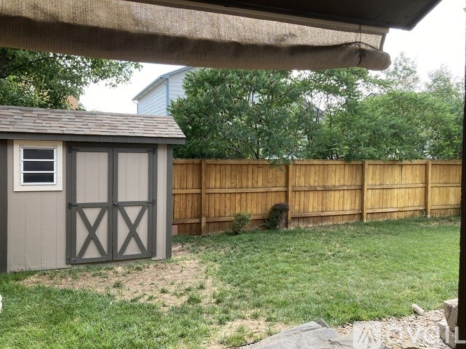 A small shed with a grey roof and brown fence.