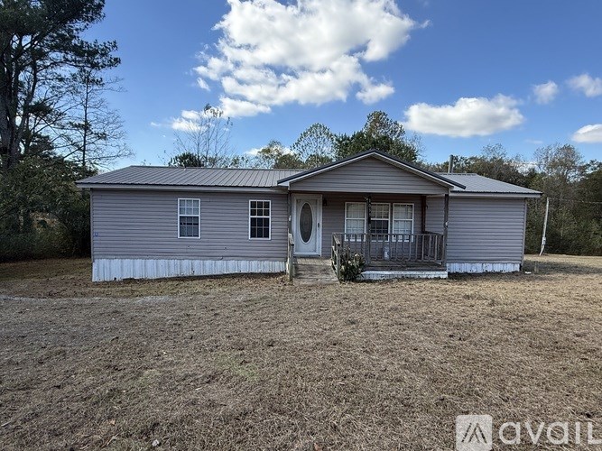 A house with a grey roof and white trim is surrounded by a dry grass field.