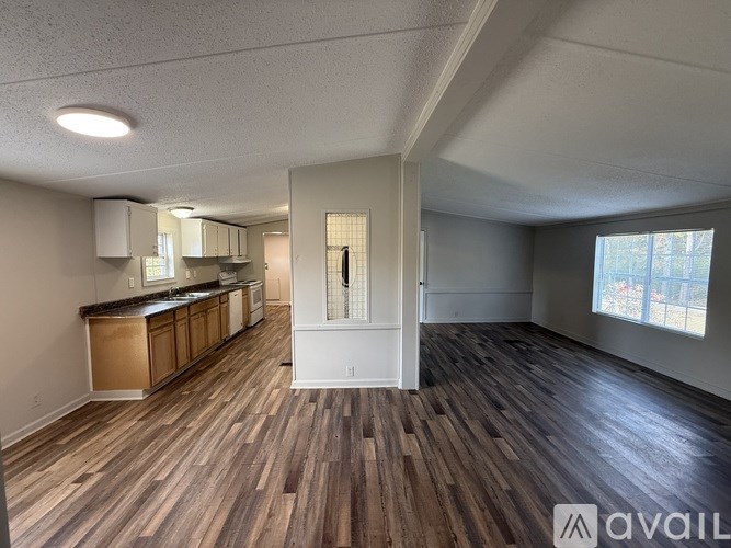 A spacious room with wooden flooring and a kitchen area with white cabinets.