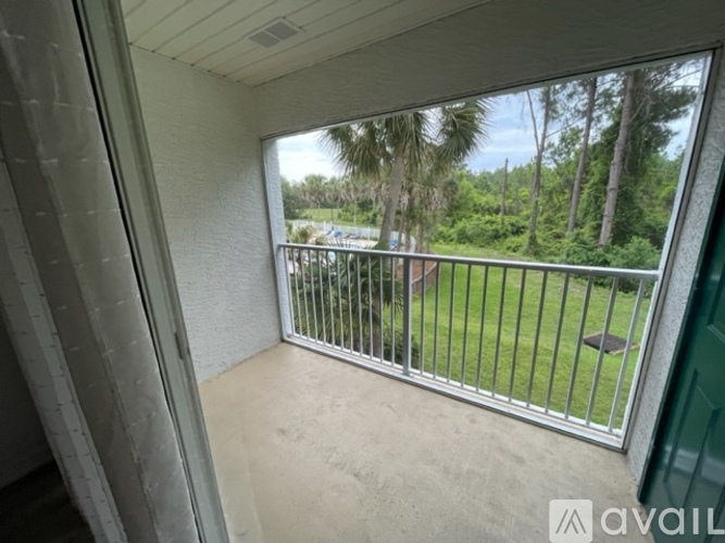 A balcony with a metal railing overlooks a grassy area with trees.