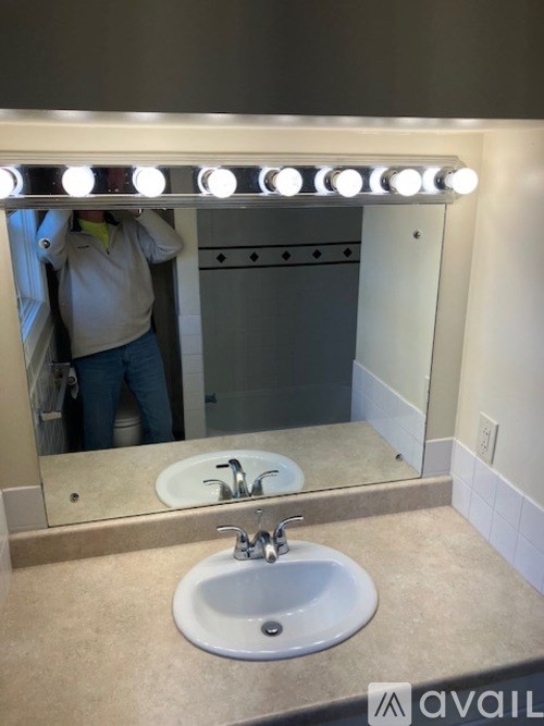 A man is standing in front of a bathroom mirror with lights on it.