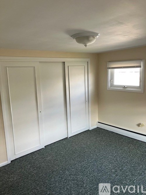 A room with a grey carpet and a window with blinds.