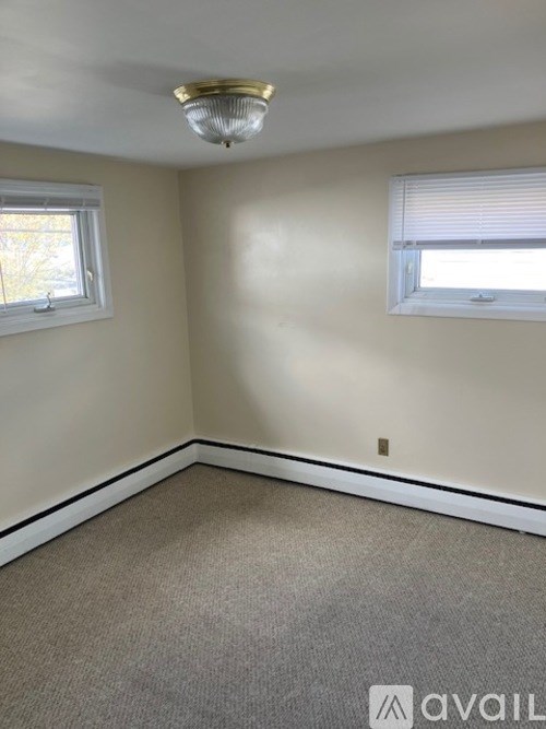 A room with a carpeted floor, a window with blinds, and a ceiling light fixture.