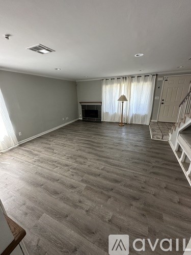 A spacious room with wooden flooring and a staircase on the right side.
