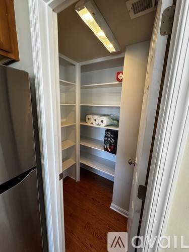 A kitchen pantry with a refrigerator on the left and a white door on the right.