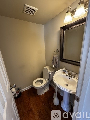 A bathroom with a toilet, sink, mirror, and light fixture.