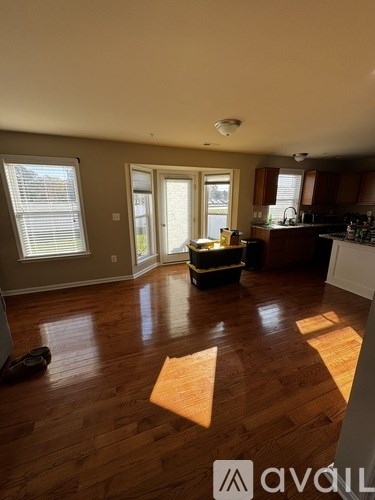 A room with wooden floors and a kitchen area in the background.