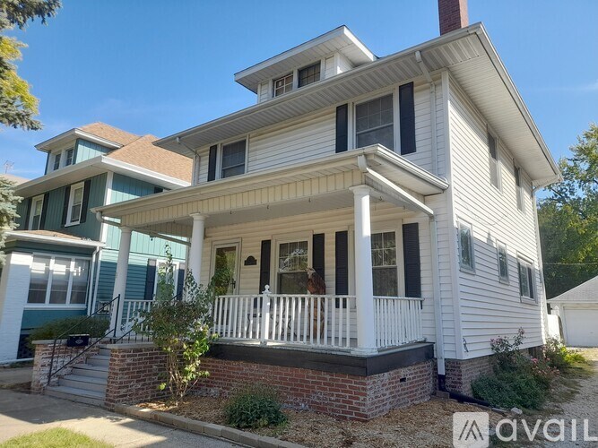 A white house with a porch and a brick base.