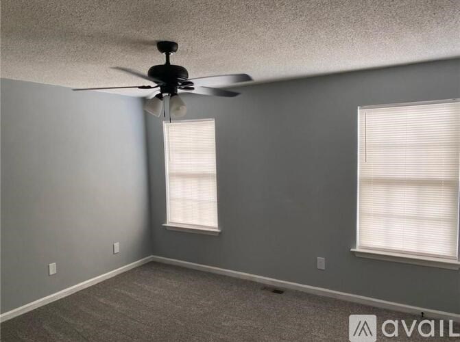 A room with a ceiling fan and two windows.