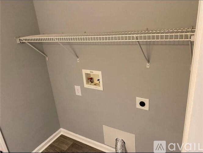 A white shelf is mounted on a wall with a small picture frame and a vent below it.