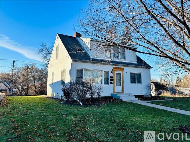 A white house with a black roof and a yellow door is surrounded by a grassy lawn.