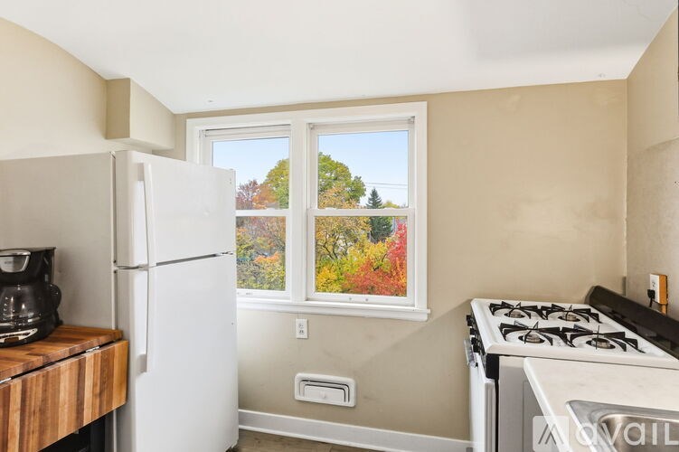 A kitchen with a white refrigerator, a stove, and a window with a view of trees.