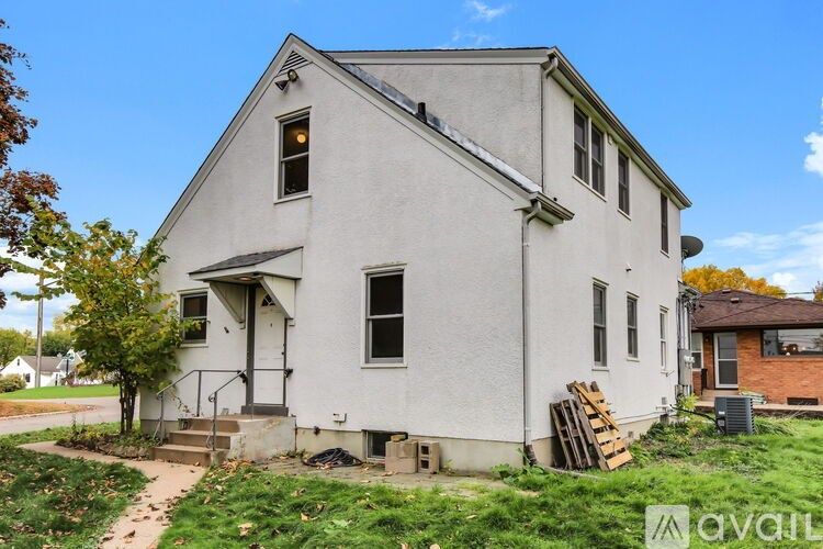 A white house with a brown roof and a tree in front.